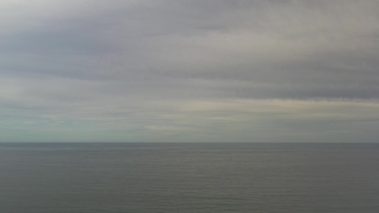 Los Cabos, Mexico ocean horizon with muted blue-green water, a low band of haze, layered gray clouds, and no visible people.