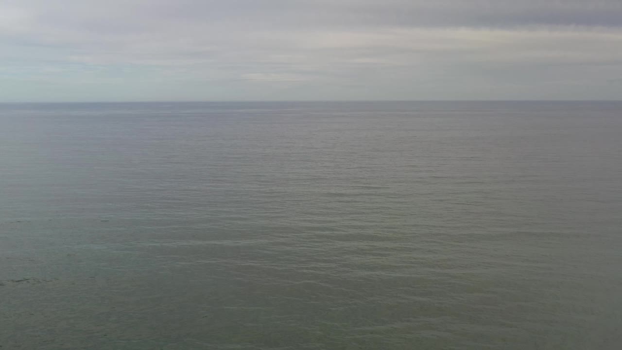 High aerial frame in Los Cabos showing open ocean with fine ripples, a soft gray-blue sky band, and no visible people or vessels.