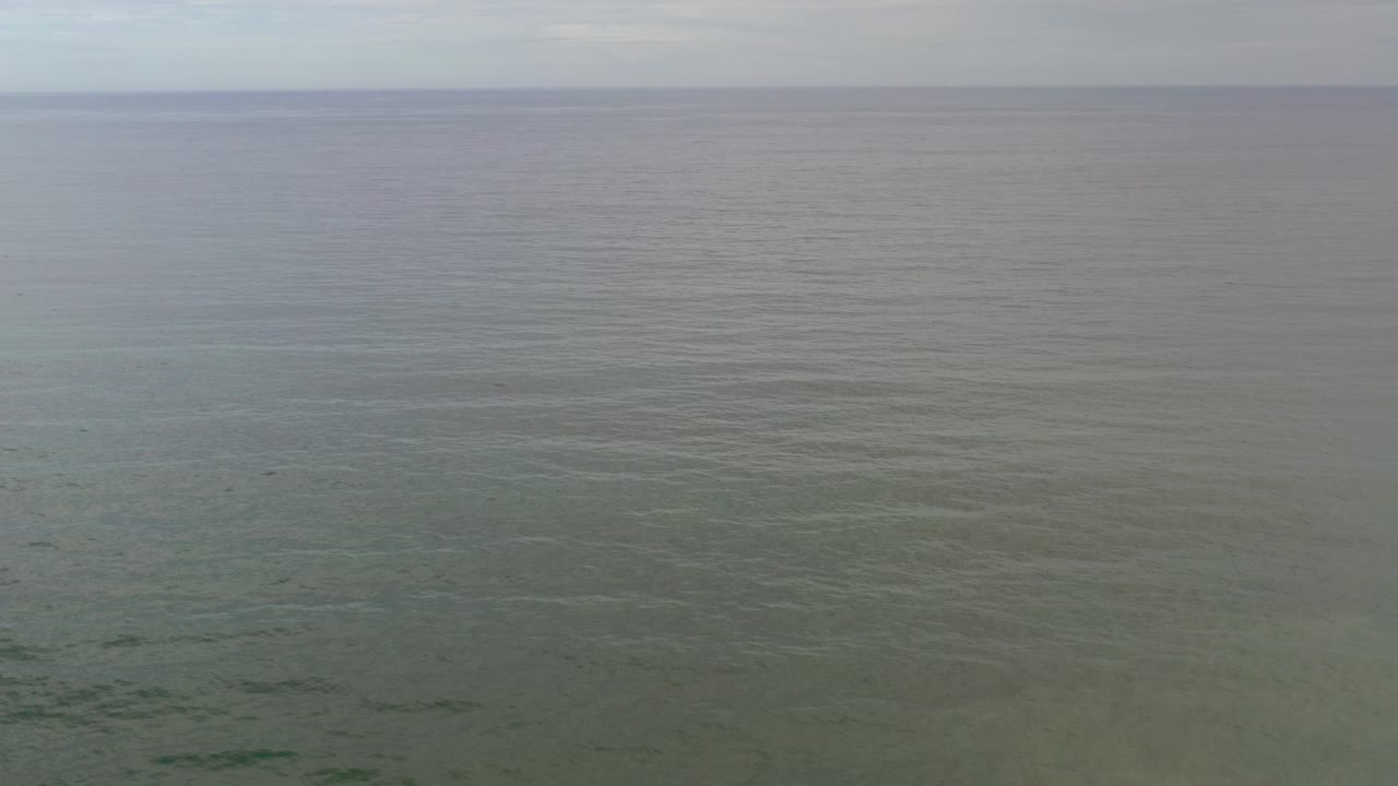 Wide aerial view of ocean under pale sky.