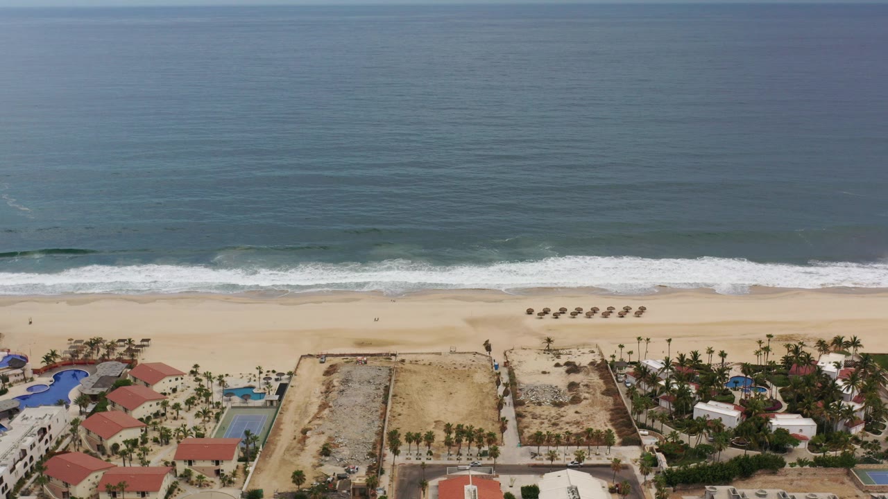 Aerial view of ocean waves reaching a sandy beach with coastal buildings below.