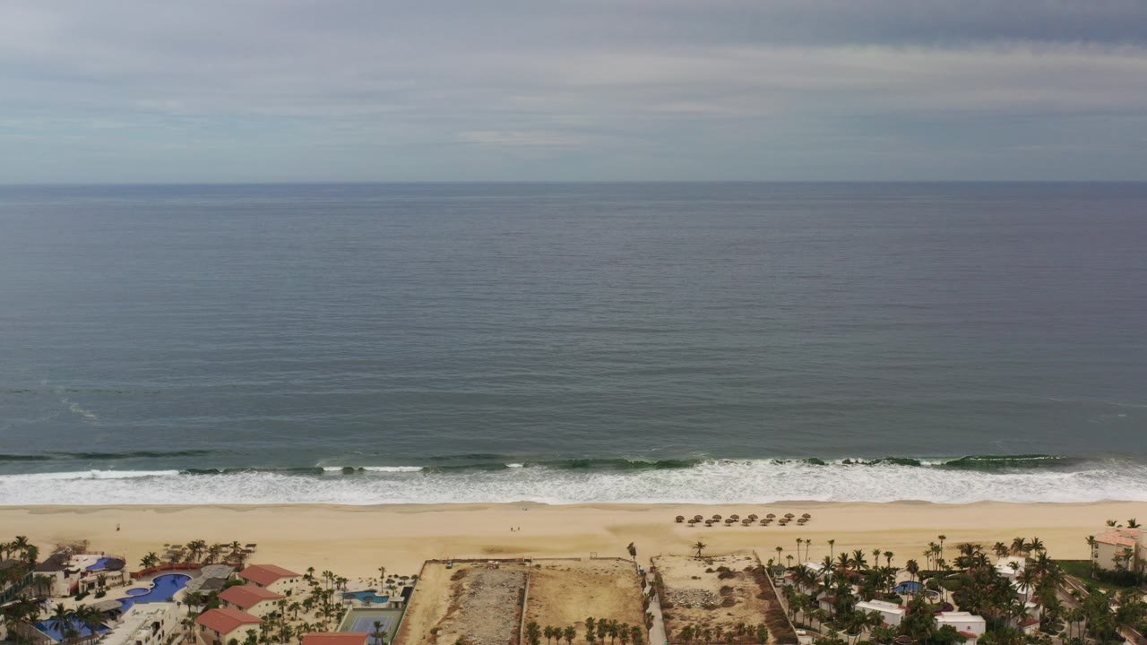 Wide aerial coast with ocean, surf, beach, and cloudy sky.