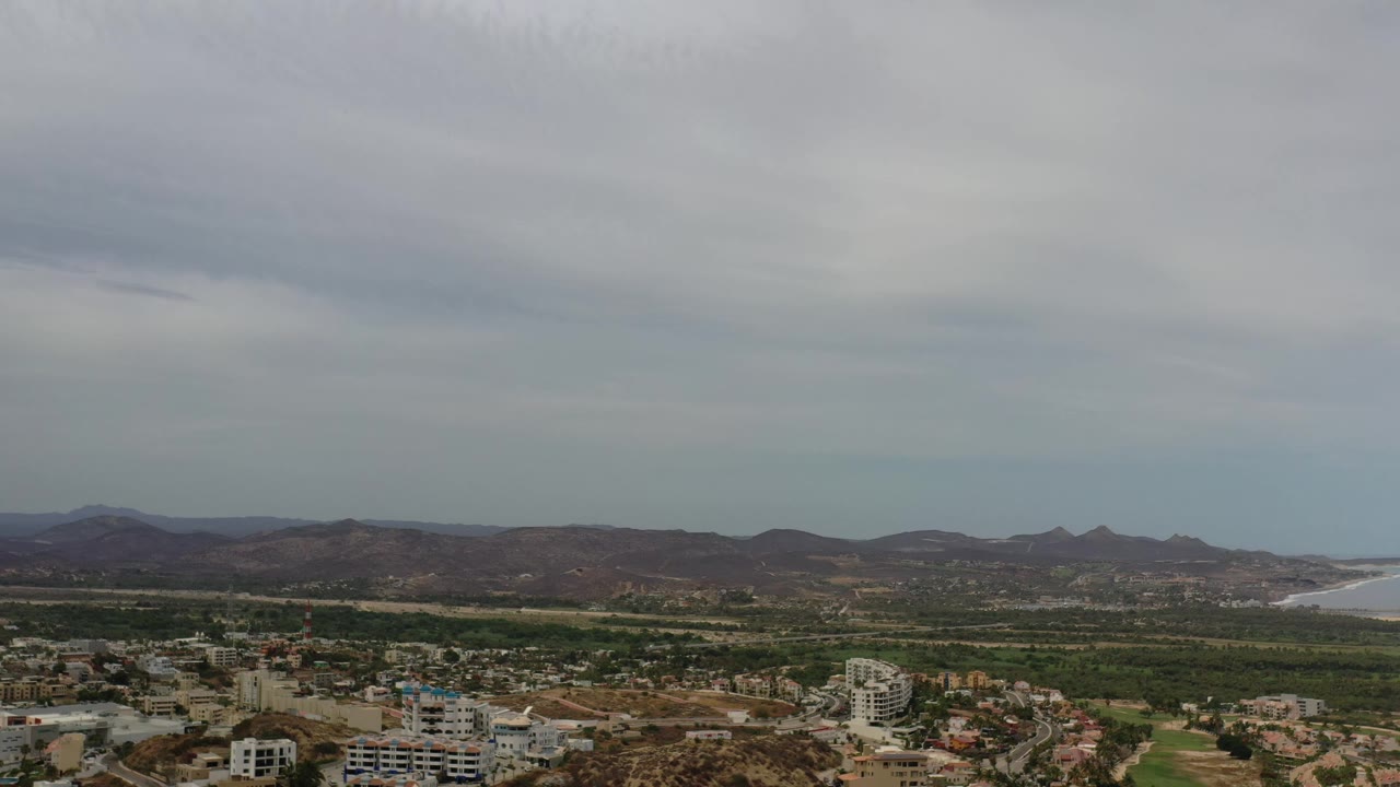Wide aerial over Los Cabos with buildings below and coastline to the right.