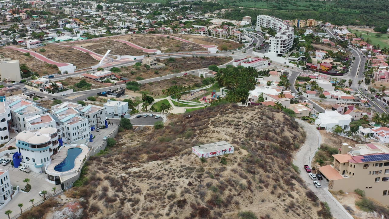 High aerial of a dry hillside beside villas, roads, parked cars, and town blocks.