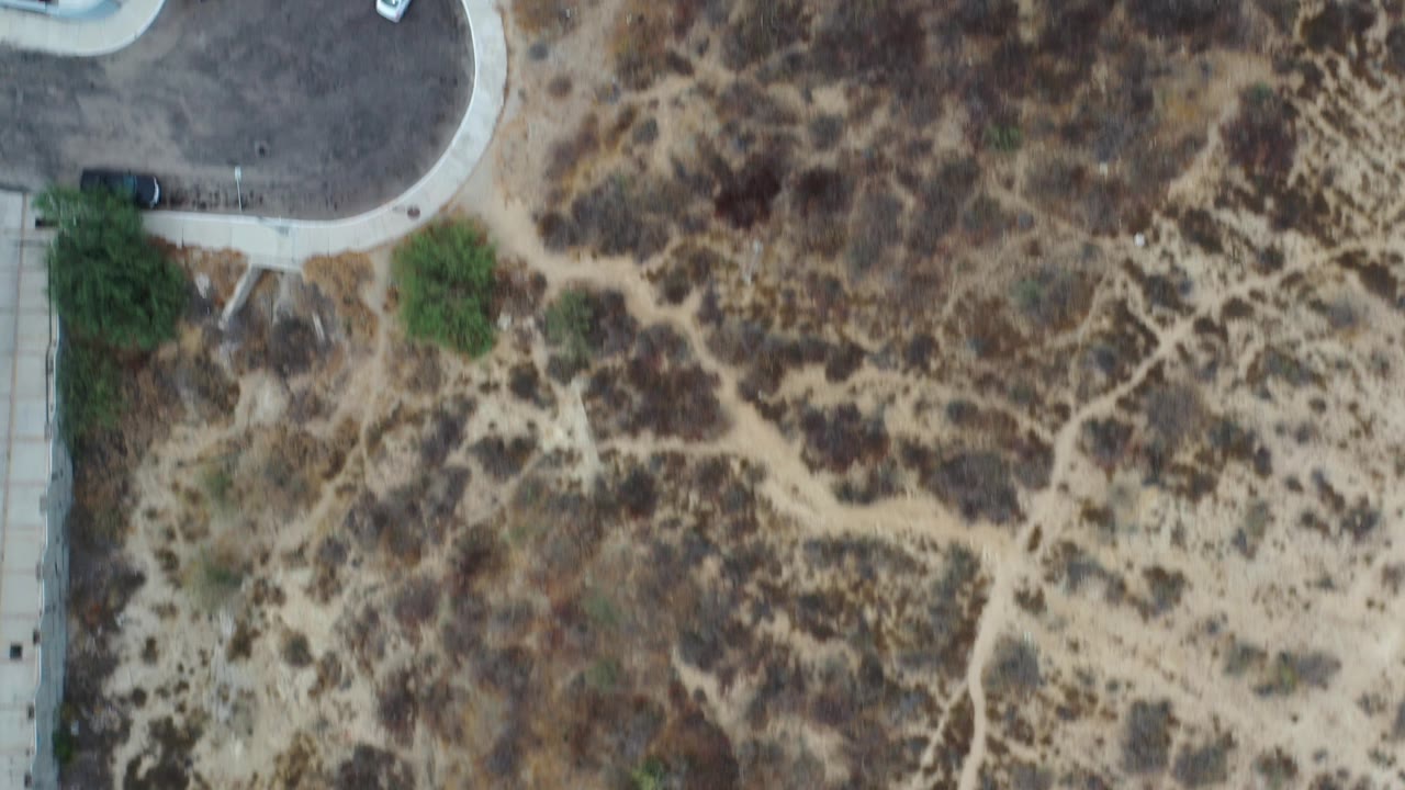 Top-down aerial view of a rounded parking area beside dry scrub ground.