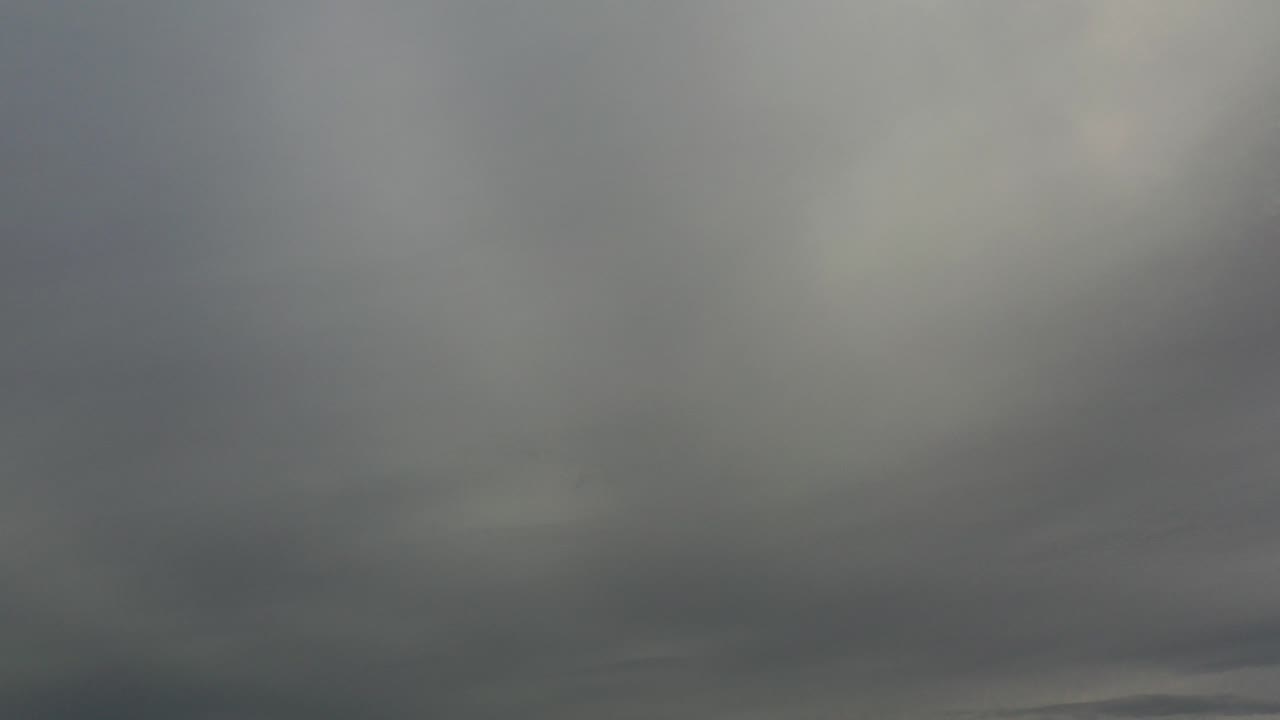 Early frame from Los Cabos, Mexico showing layered gray clouds across the sky with only a very low, faint horizon line and no visible people.