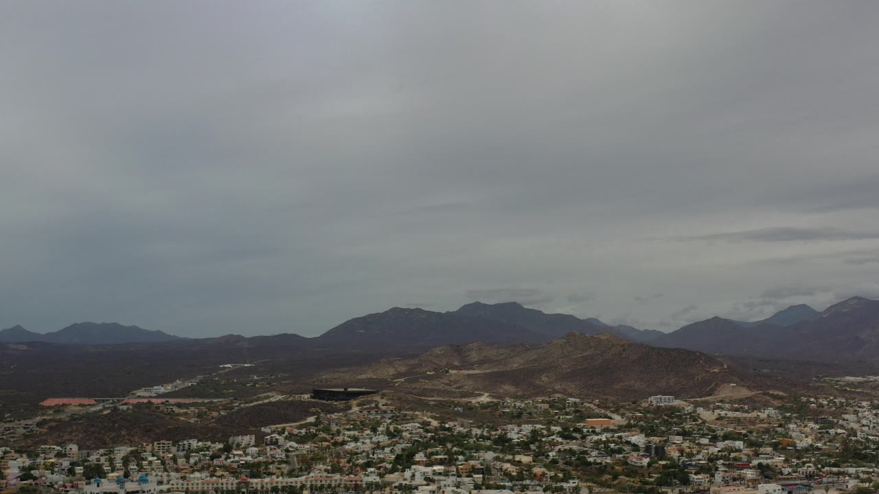 Aerial view of a city below brown mountains and gray clouds.