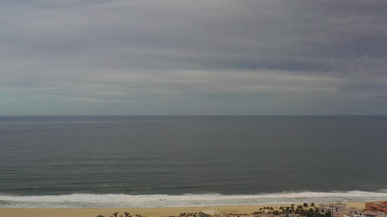 Wide ocean horizon beneath dark gray clouds with surf and beach below.