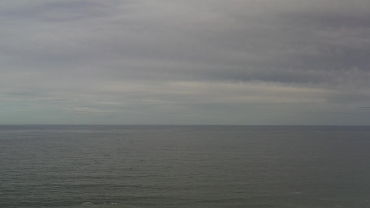 Wide Los Cabos ocean view at the start of the clip, with gray-green water below a layered overcast sky and no visible people.