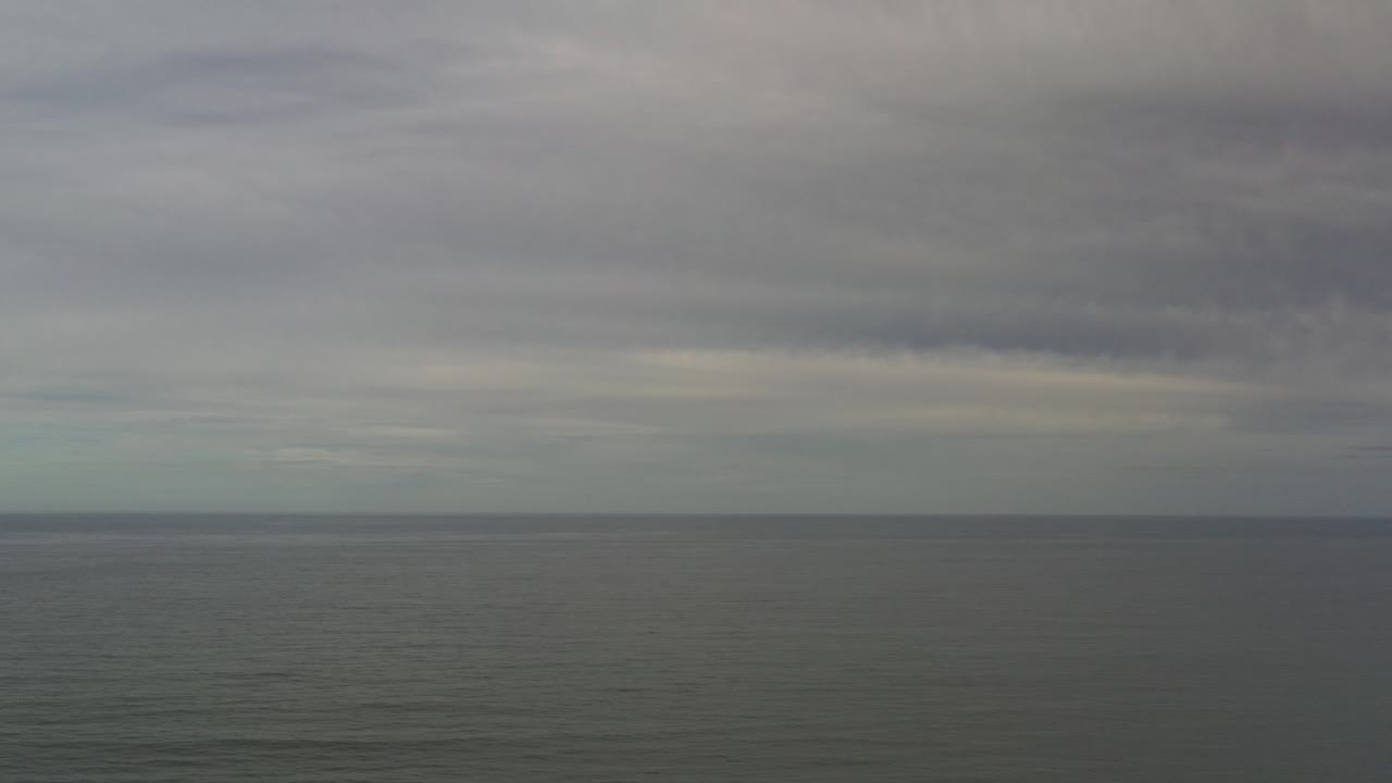 Opening frame of the Los Cabos Mexico clip with a level gray ocean horizon, heavy cloud bands, muted water, and no visible people.