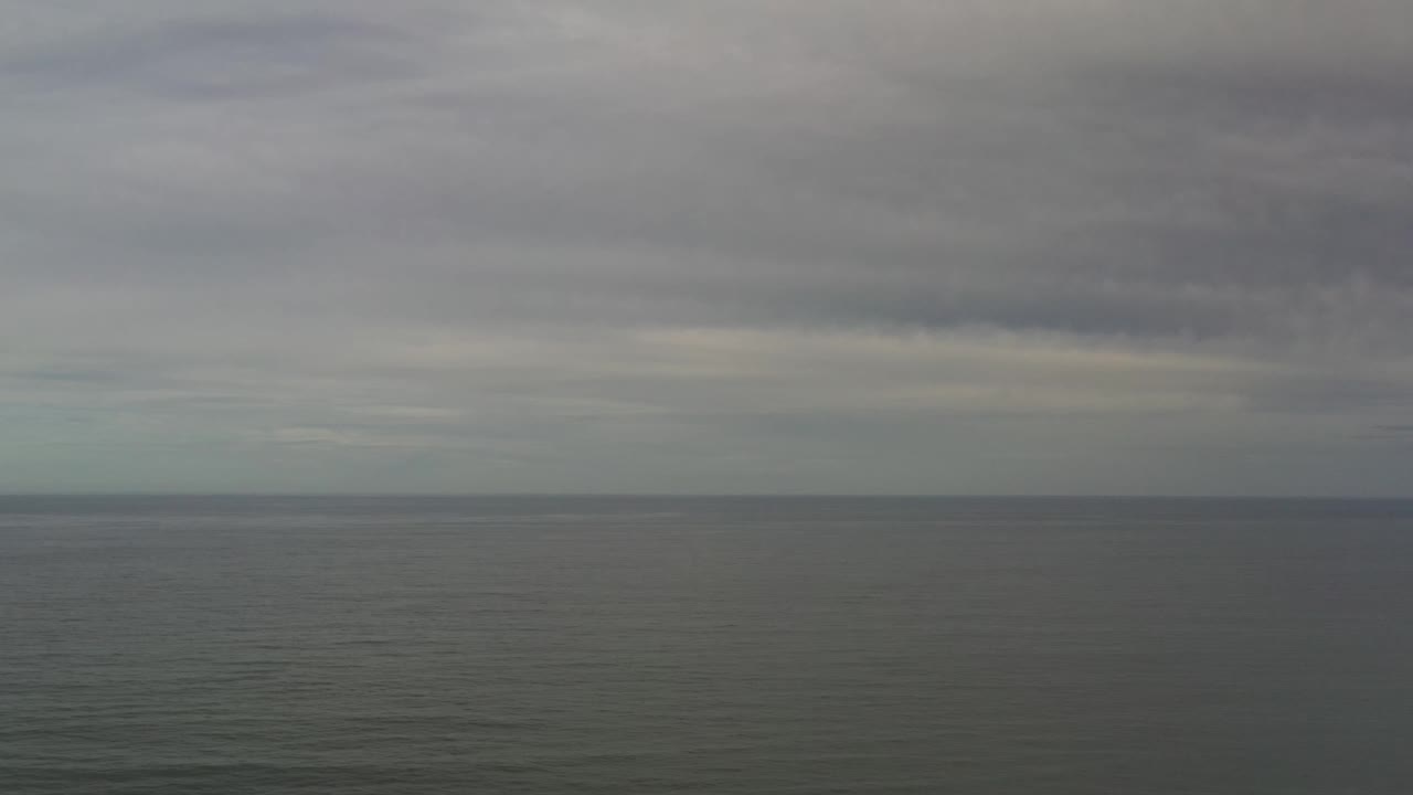 A wide Los Cabos sea view shows the horizon beneath dense gray clouds, with faint surface ripples and no visible people.