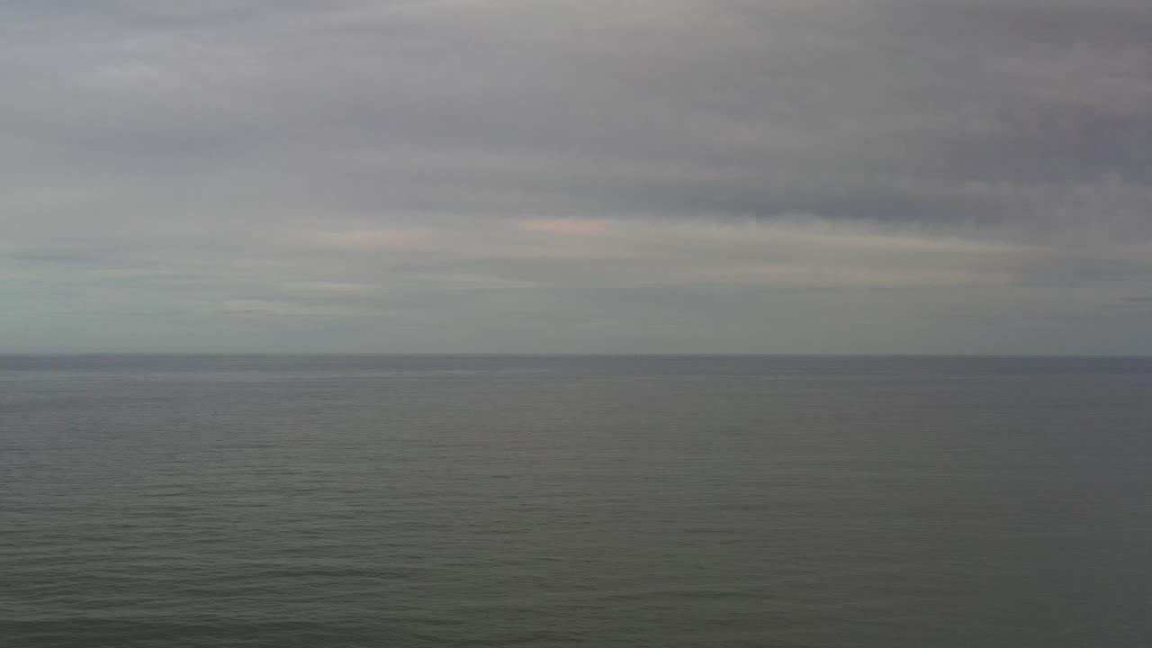 Flat Los Cabos sea horizon with layered gray clouds and a faint pale strip of light near the skyline, with no visible people.