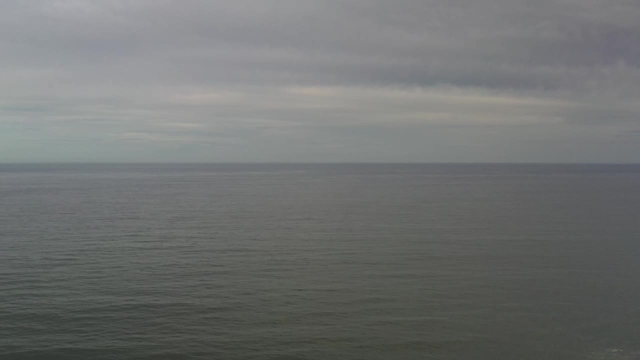 Open Los Cabos ocean water fills the frame beneath a muted cloudy sky, with the horizon running nearly straight across and no visible people.