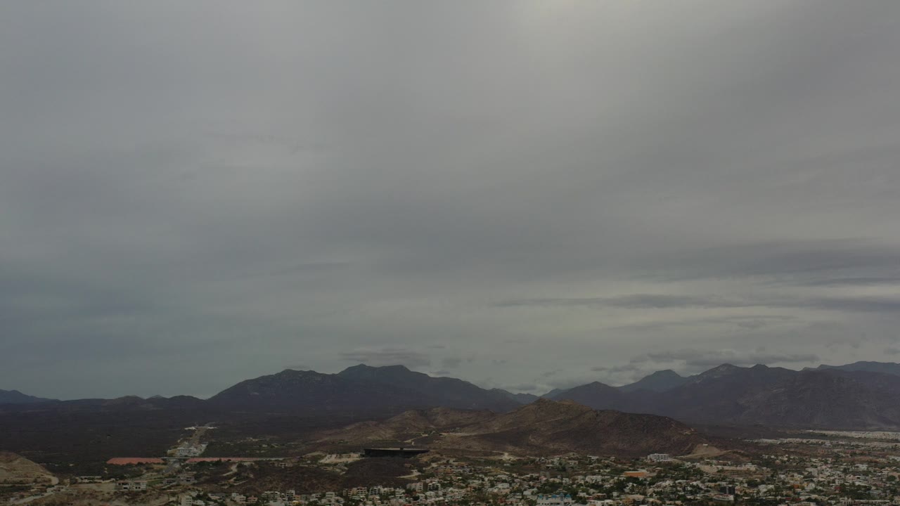 Cloudy aerial view over city buildings, hills, and mountains.