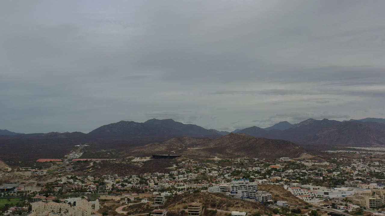 Aerial view of a town below dark mountains and gray clouds.