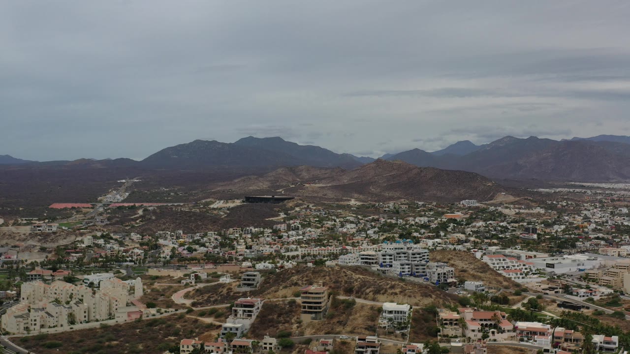 Aerial panorama of roads and buildings spreading across dry hills toward mountains.