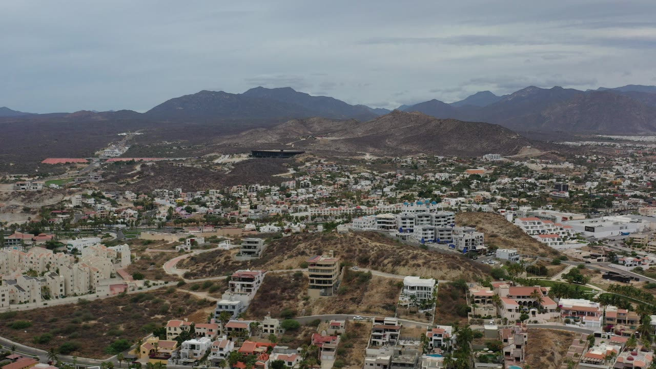 Wide aerial view of hillside homes, roads, dry terrain, and distant mountains.