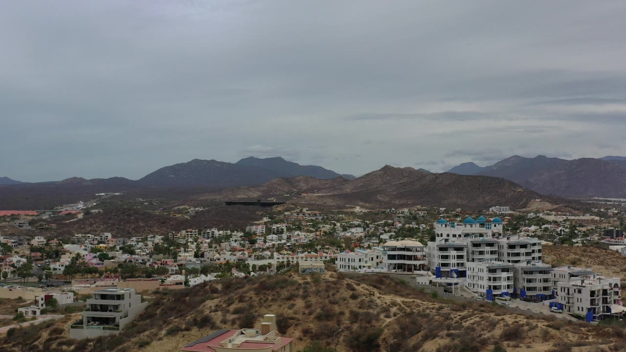 Residential hillside and mountains under a gray cloud layer.