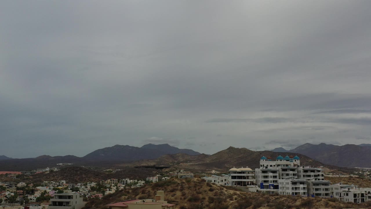 Residential hillside and mountain range beneath an overcast sky.