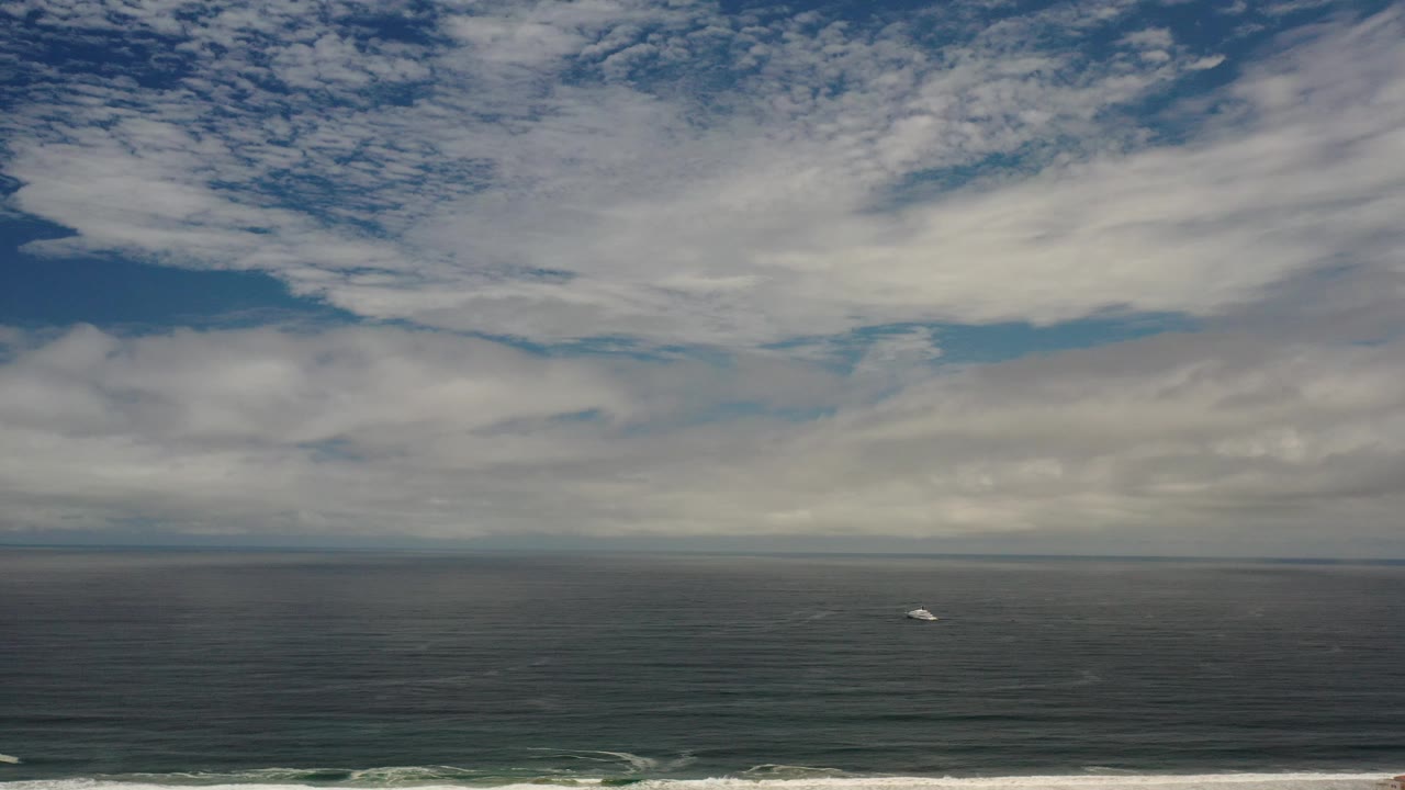 Elevated view of ocean, cloudy sky, surf, and coastal houses.