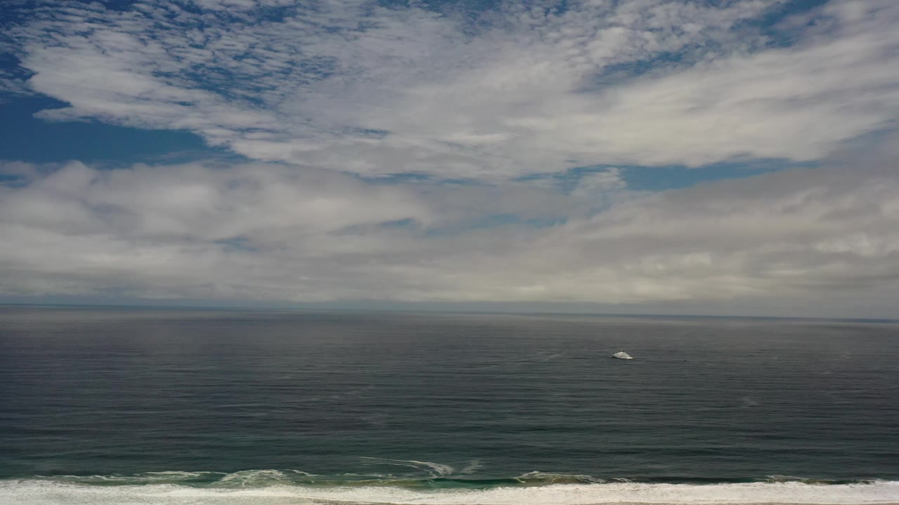 Cloudy coastal aerial over green ocean with a distant white boat.