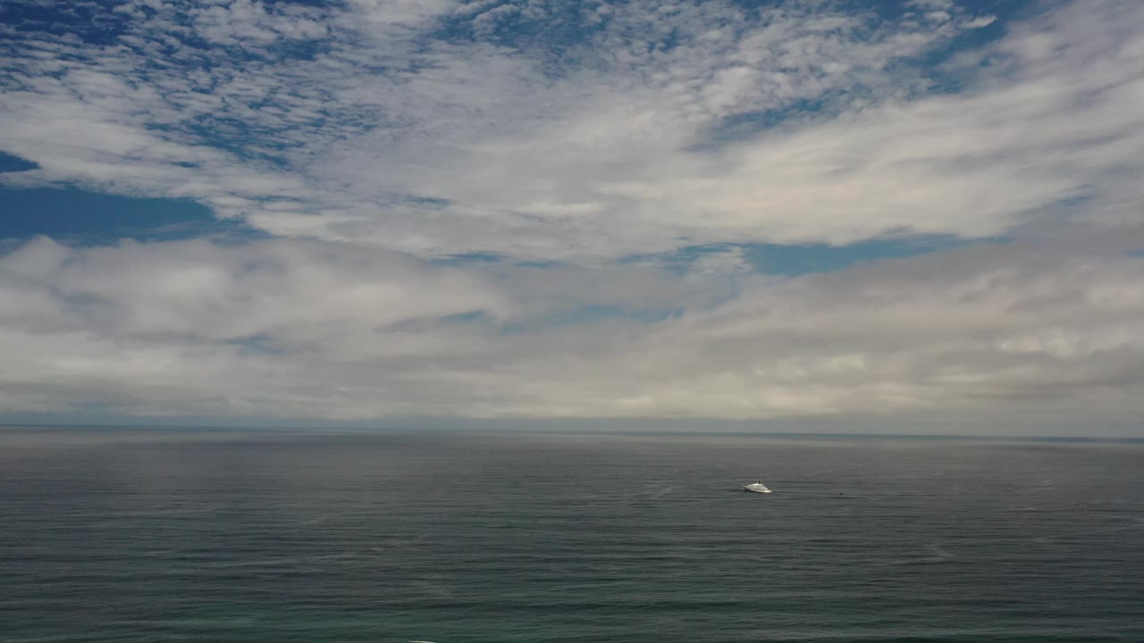 Open water and a distant white boat beneath streaked clouds and blue sky.