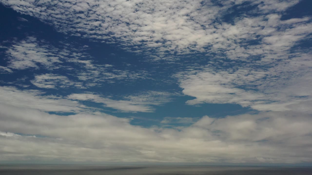A wide Los Cabos, Mexico sky view with broken white clouds over a thin dark ocean horizon and no visible people.