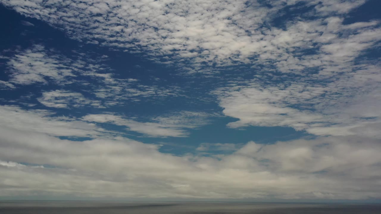 The Los Cabos coastal view shows textured cloud layers across blue sky, with the ocean horizon sitting low and no visible people.