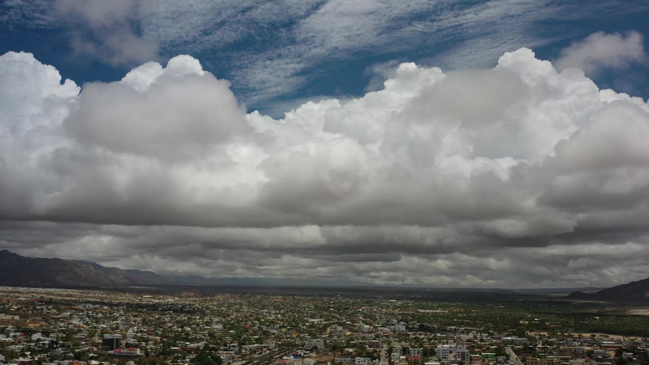 Bright cumulus clouds hang over city, open land, and mountains.