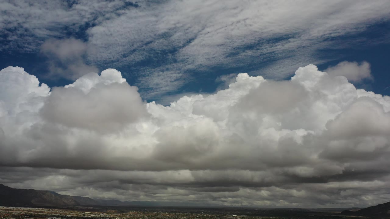 Bright cumulus clouds above arid terrain and mountains
