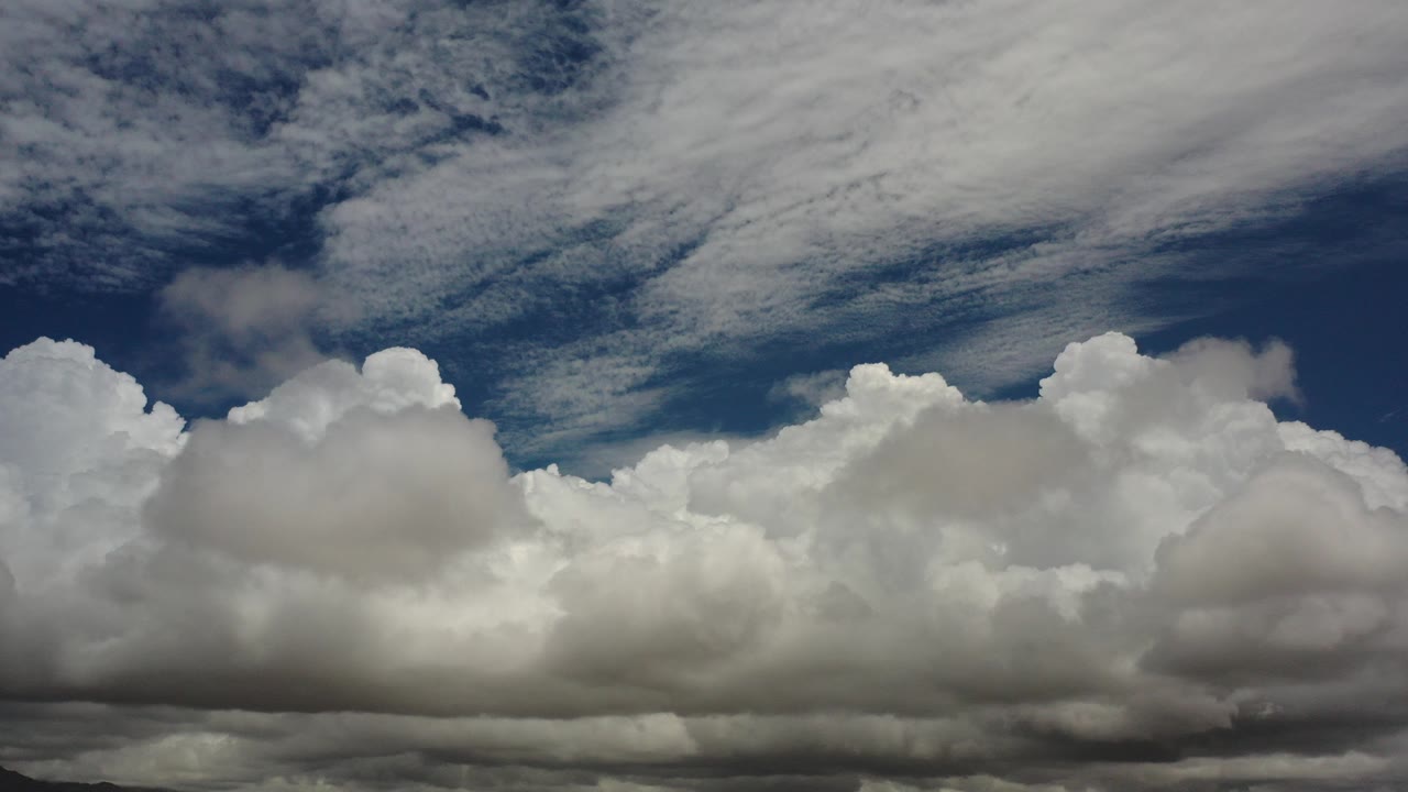 Opening frame of white cumulus clouds under thin stratus streaks in a blue Los Cabos sky, with no visible people.