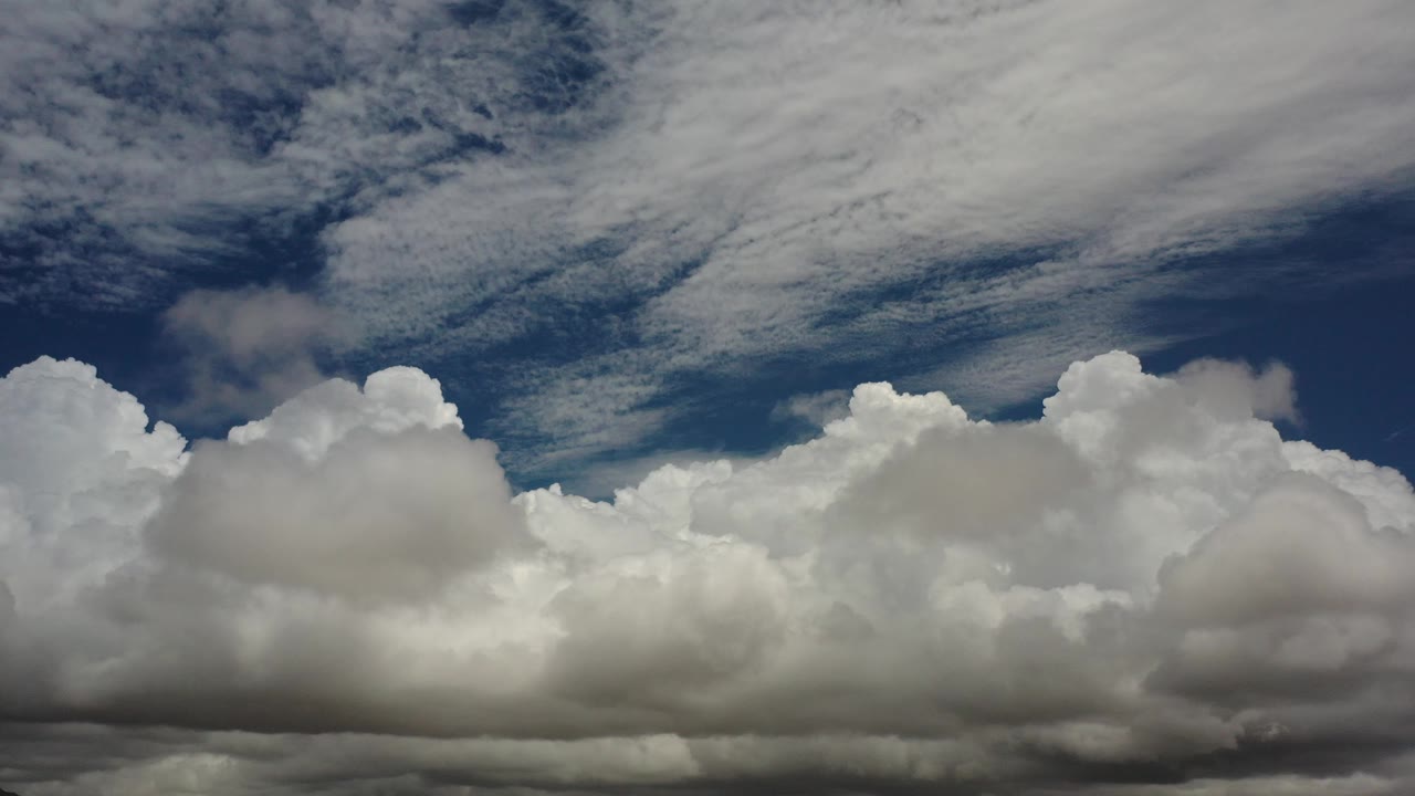 Layered cumulus clouds and high streaks across deep blue sky.