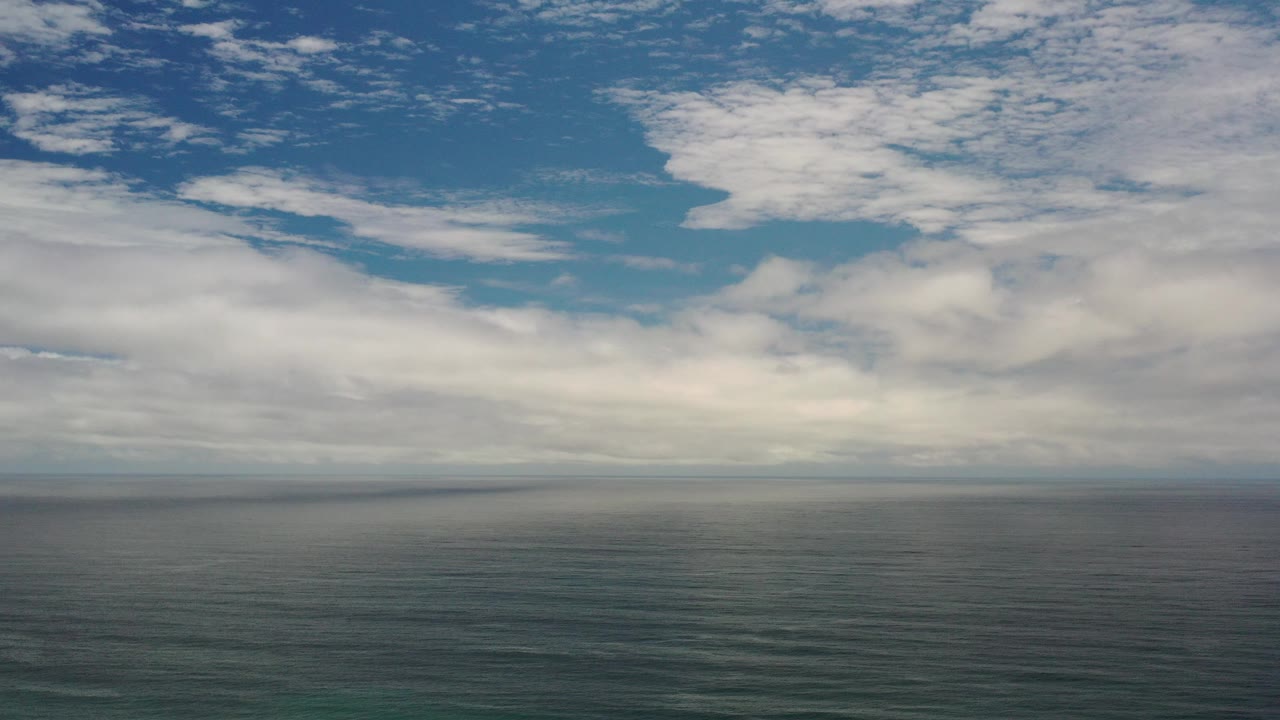 Wide ocean horizon beneath layered white clouds and blue sky.