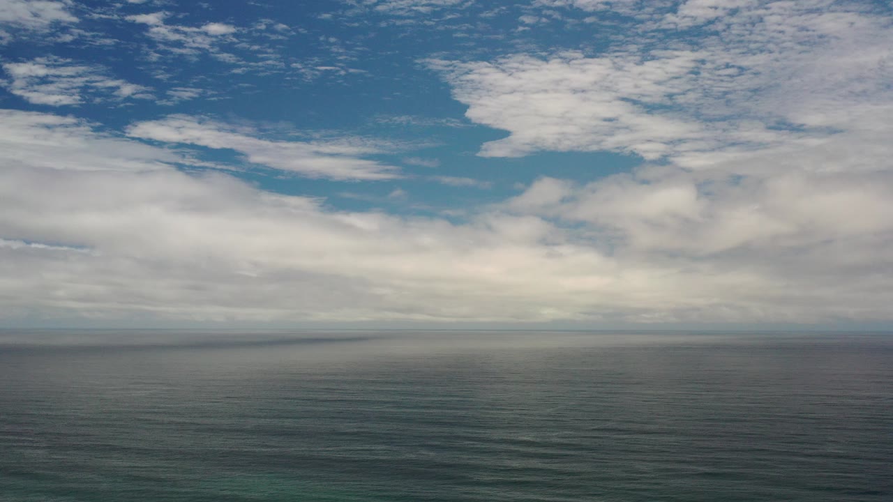 Opening frame of Los Cabos, Mexico ocean with a level horizon, layered clouds, muted teal water, a thin surf edge, and no visible people.