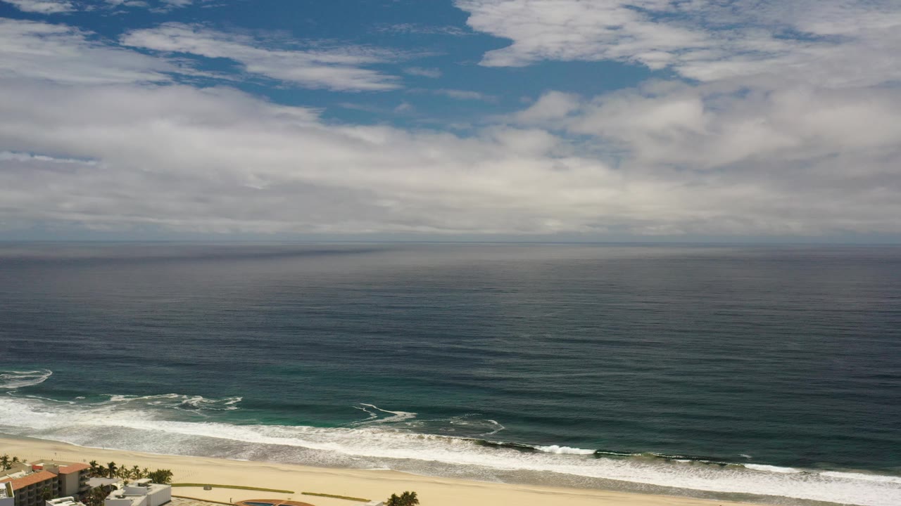 Cloudy sky over ocean surf and beachfront buildings at the bottom edge.