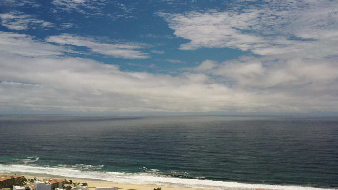 Wide ocean horizon under layered clouds with surf at the lower edge.