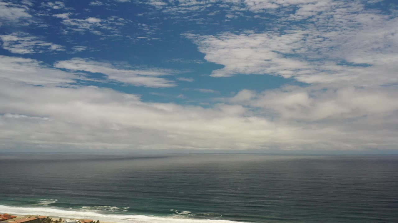 Blue ocean and broad cloud cover with white surf along the lower edge.