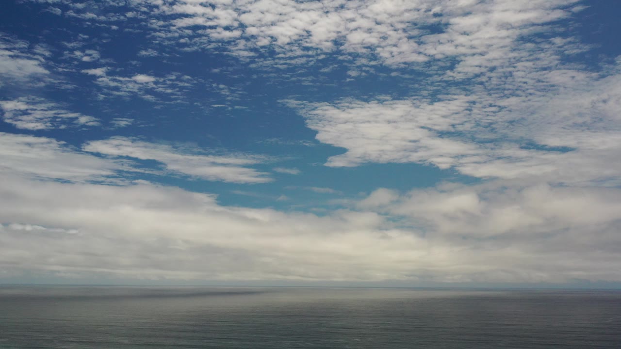 Opening frame of the Los Cabos, Mexico clip showing scattered white clouds across blue sky above a thin dark horizon, with no visible people.