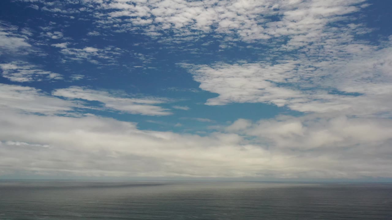 Los Cabos sky frame with a broad white cloud shelf near the horizon and patchier clouds higher in the blue sky, with no visible people.