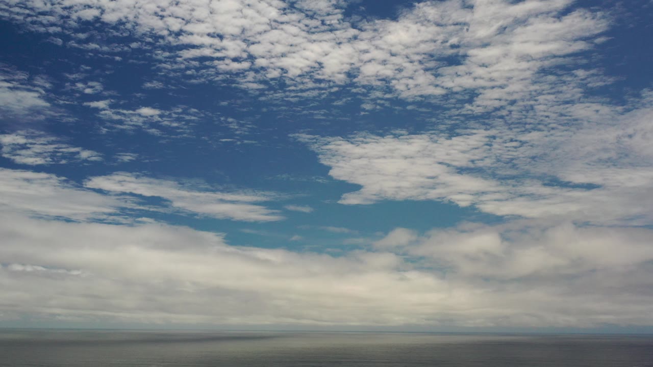 Opening frame of a Los Cabos, Mexico sky view with broken white clouds across deep blue sky, a thin distant horizon, and no visible people.