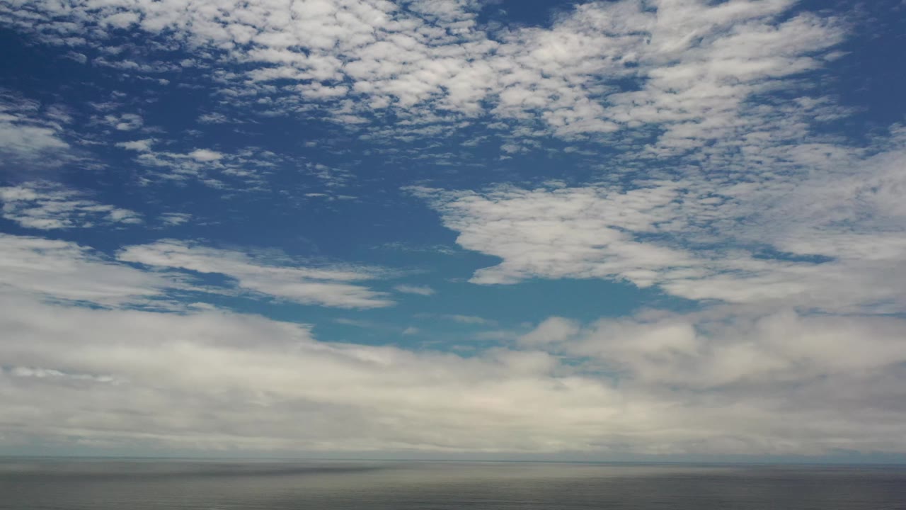 Second frame from the Los Cabos sky clip, showing thicker cloud bands near the horizon and scattered smaller clouds across the upper blue sky, with no visible people.