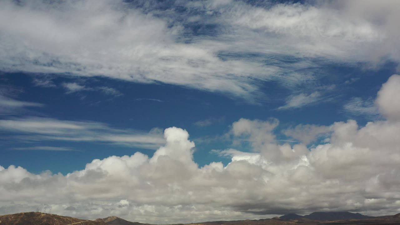 Large cumulus clouds over a thin distant land horizon.