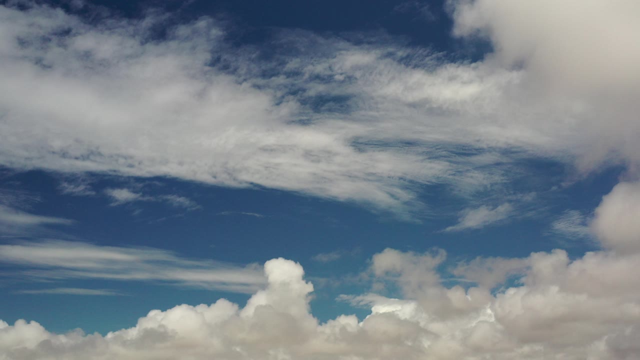 Opening frame of a Los Cabos sky view with deep blue upper sky, broad white cloud layers, lower cumulus clouds, and no visible people.