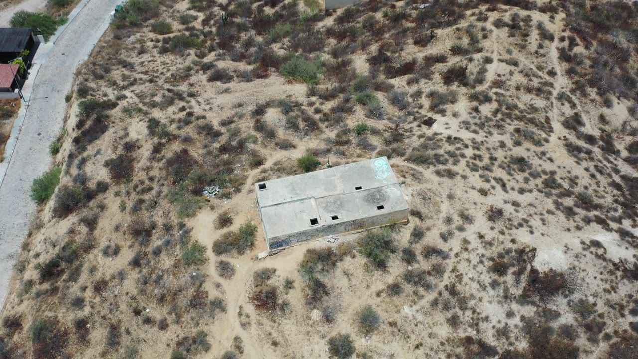 Overhead view of a lone concrete building in sandy scrubland near a paved road.