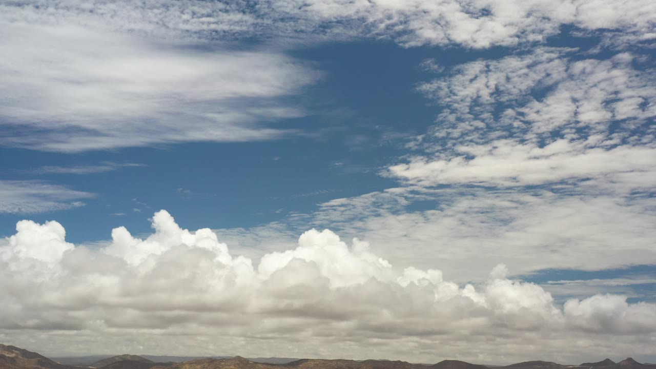 Opening frame of Los Cabos, Mexico with a deep blue sky, layered white clouds, low brown hills, and no visible people.