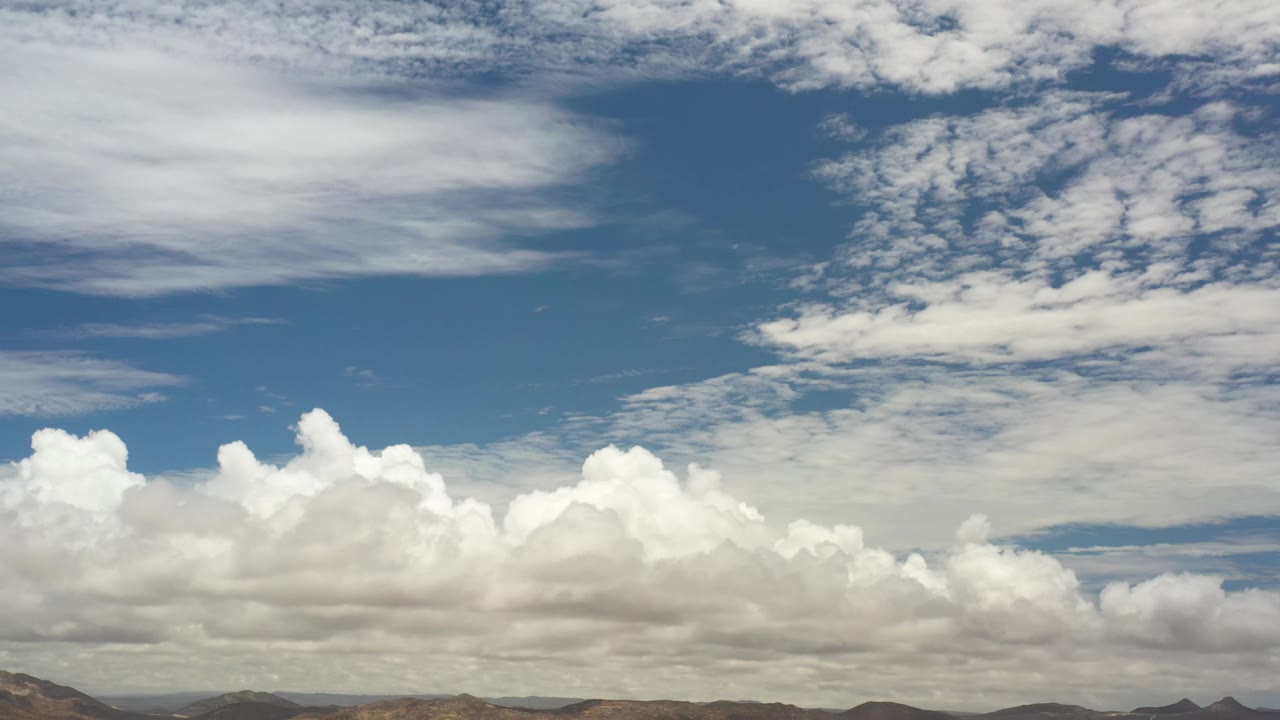 A bright cloud bank stretches across the Los Cabos horizon, with arid hills below and no visible people.