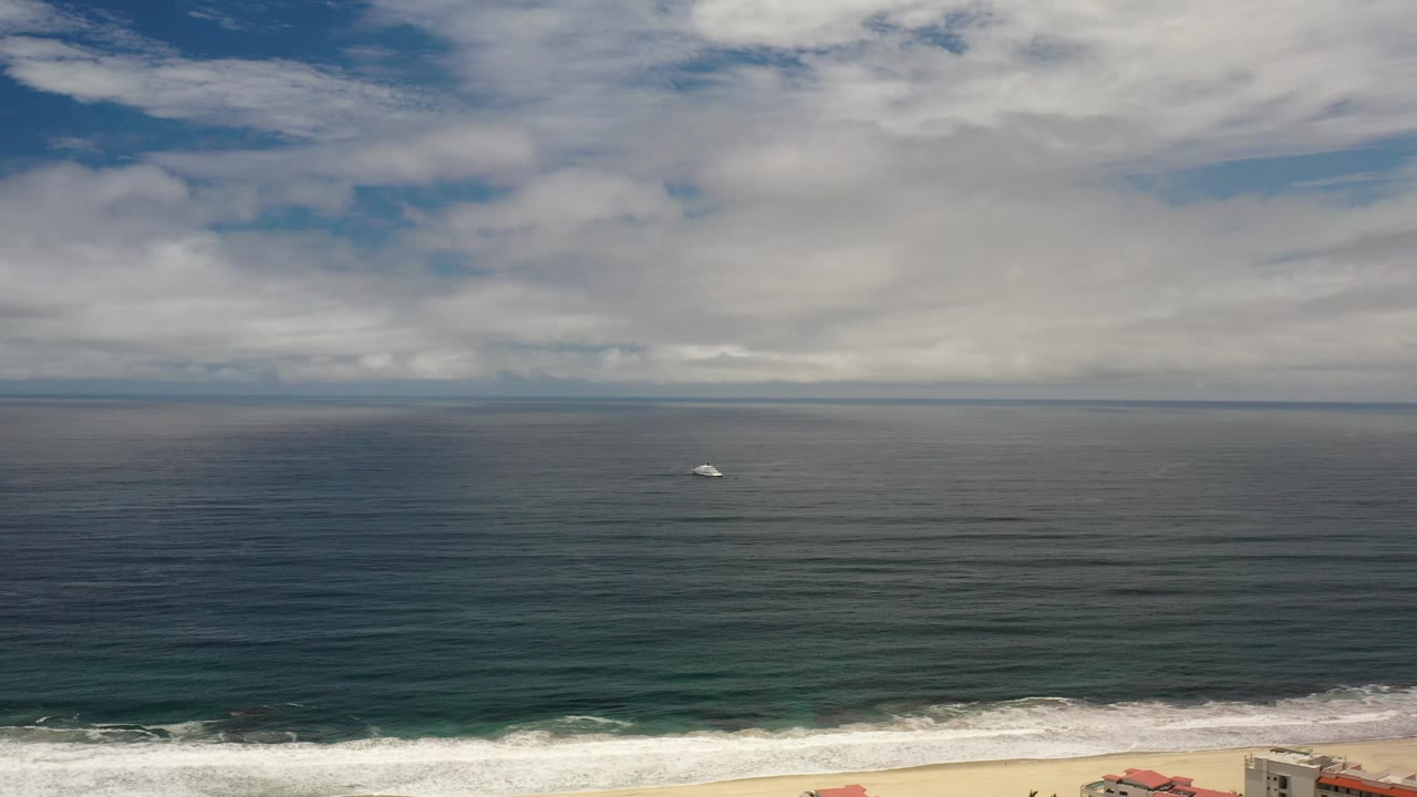 Gray ship offshore under broad clouds above green ocean.