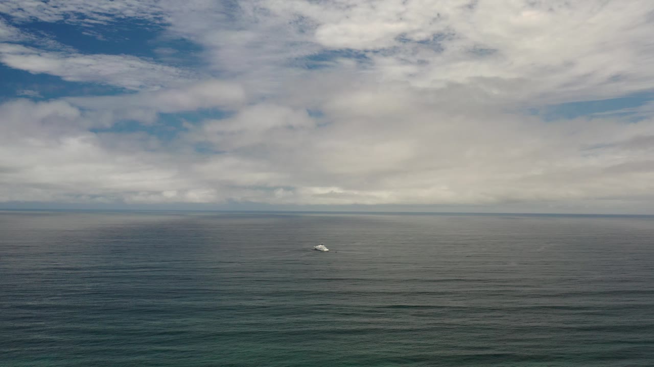 Wide Los Cabos ocean view at the start of the clip, with a small white object floating left of center beneath layered clouds and no visible people.