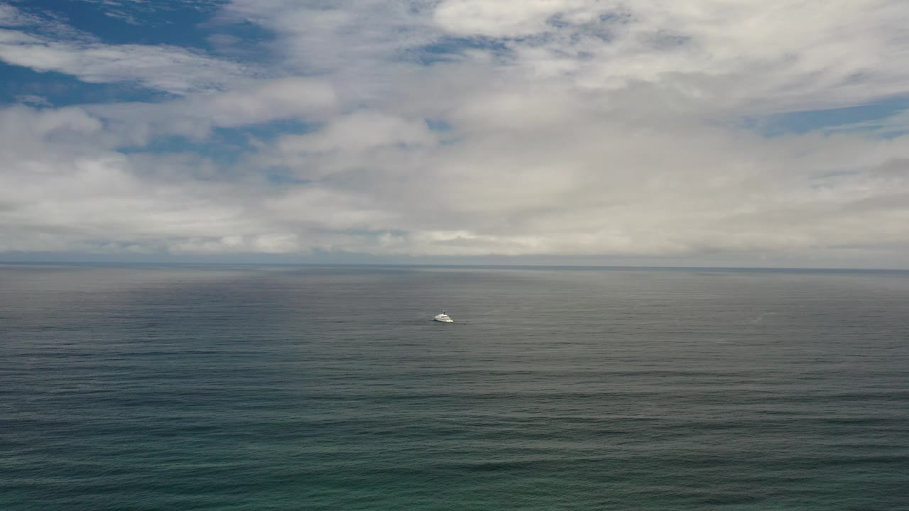 Wide Los Cabos ocean view at the start of the clip, with a tiny white boat left of center below layered clouds and no visible people.