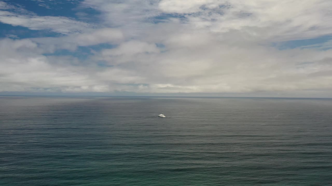 A small white boat appears slightly nearer the center of the Los Cabos seascape, with calm rippled water below a heavy cloud bank and no visible people.