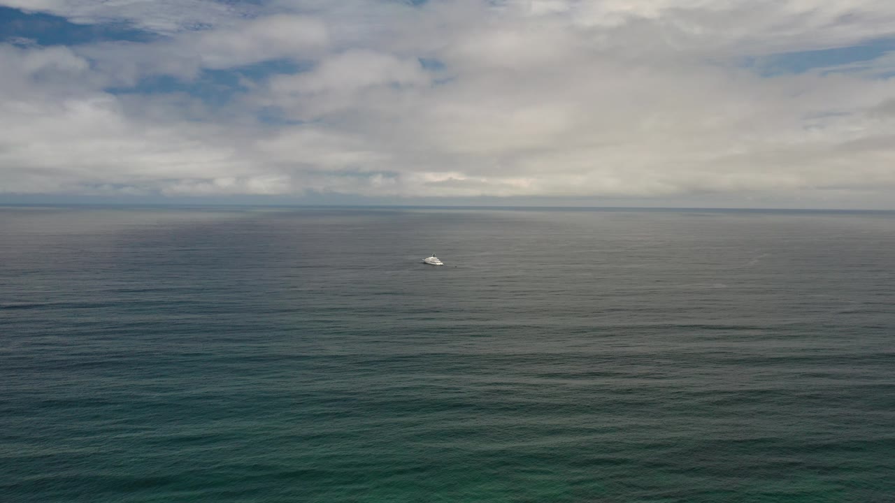 Opening frame of the Los Cabos ocean under layered clouds, with teal-gray water, a small white object near the horizon, and no visible people.
